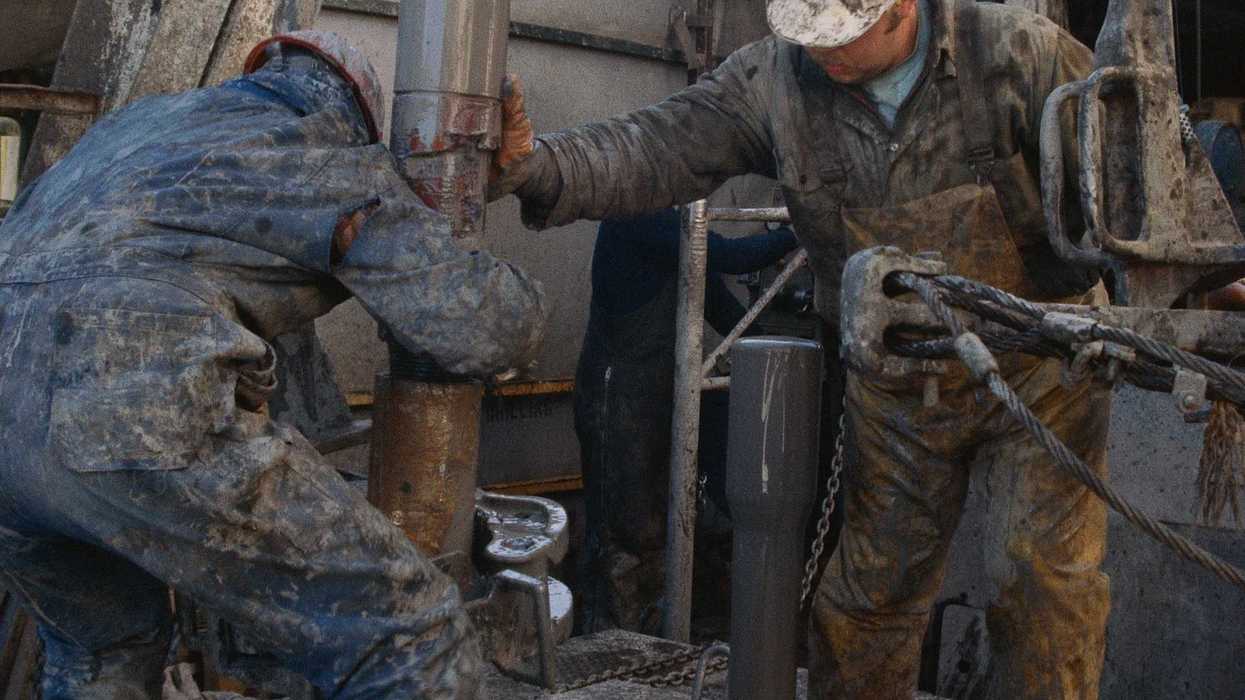 Oil field workers manipulating a drilling rig