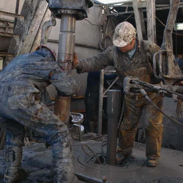Oil field workers manipulating a drilling rig