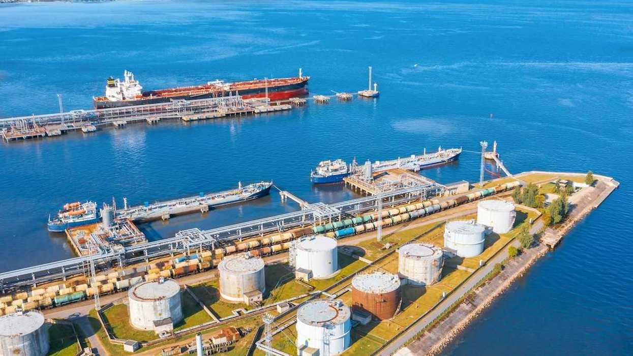 Oil tankers docking at oil terminal adjacent to multiple storage tanks.