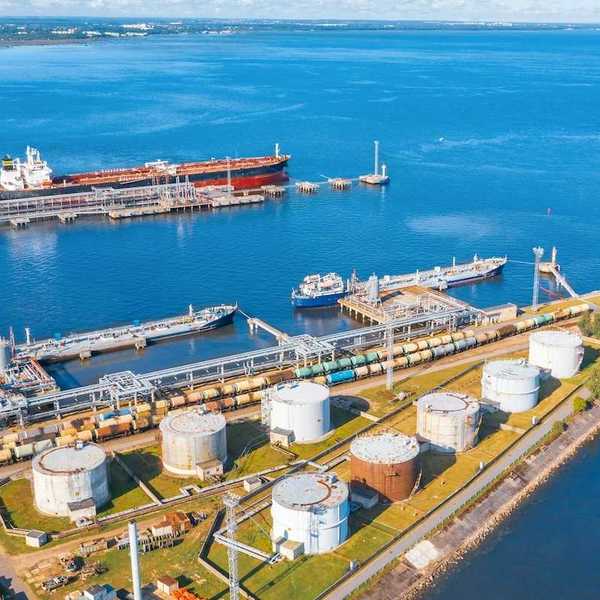 Oil tankers docking at oil terminal adjacent to multiple storage tanks.