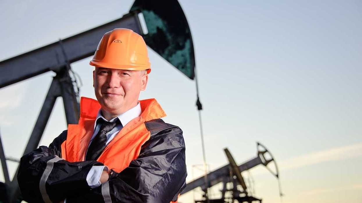 Oil worker in orange uniform and helmet on of background the pump jack and sunset sky.