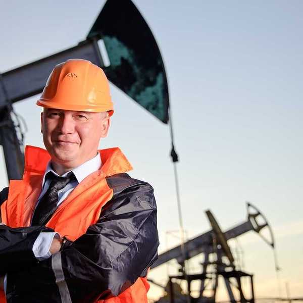 Oil worker in orange uniform and helmet on of background the pump jack and sunset sky.
