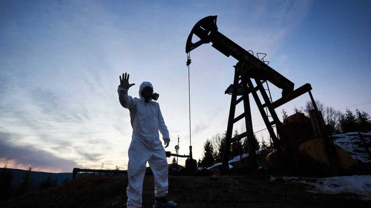 Oilfield drilling site with pump jack and worker wearing a haz-mat suit