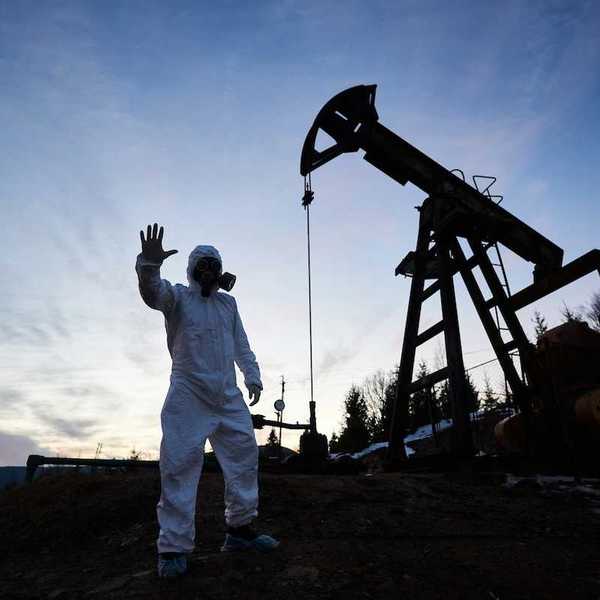 Oilfield drilling site with pump jack and worker wearing a haz-mat suit