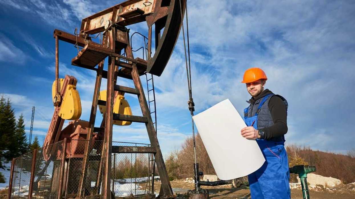 Oilfield worker standing next to a pumpjack and holding a large rectangular piece of paper