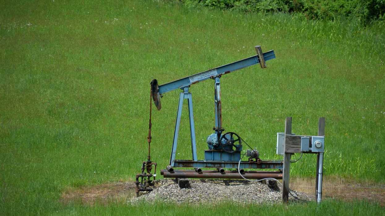 Old oil pump jack in a grassy green field.