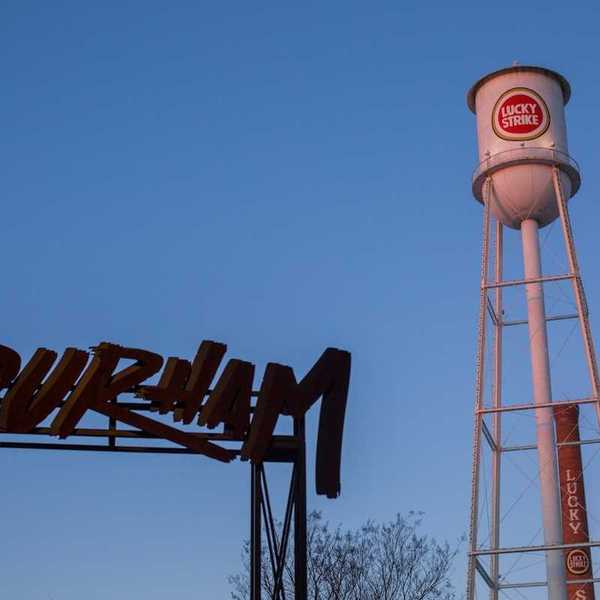 Old water tower with "Lucky Strike" logo on tank adjacent to "Durham" sign