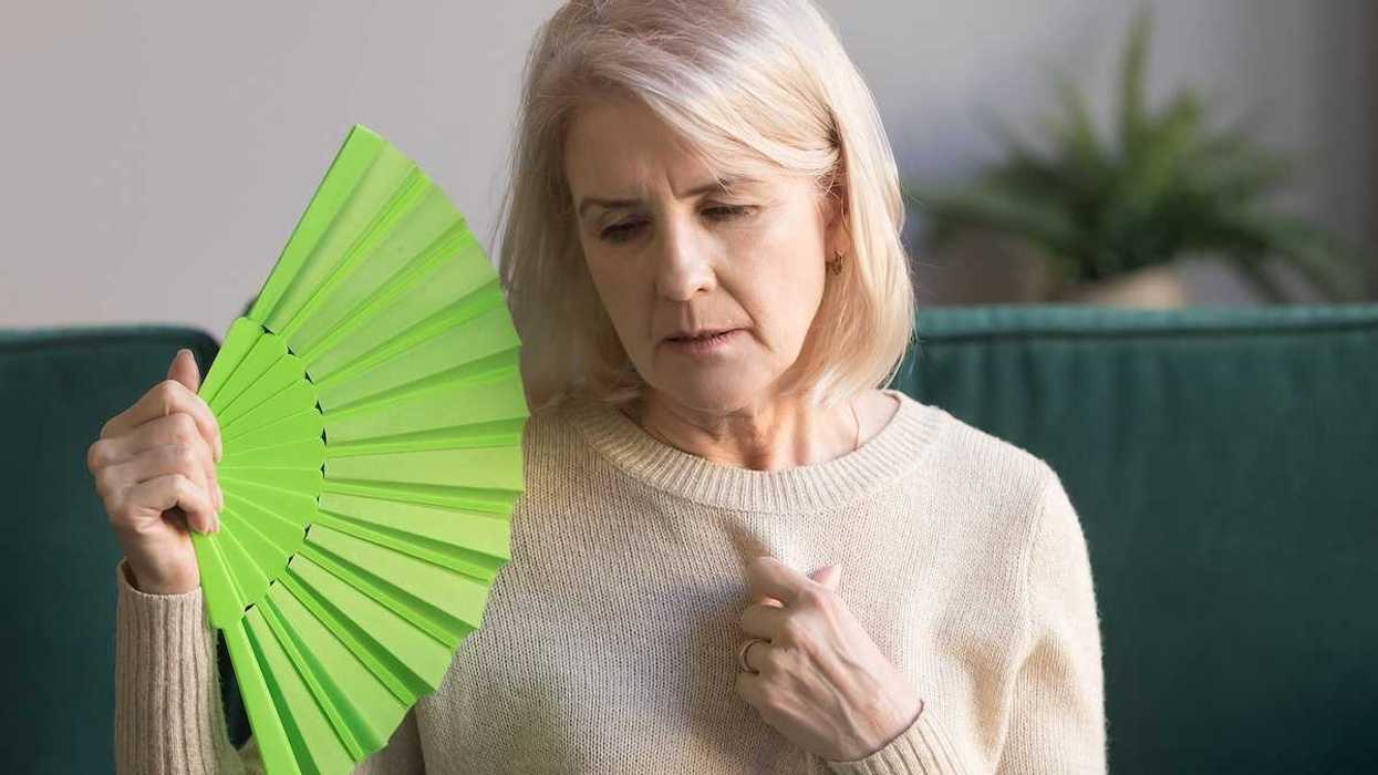 Overheated elderly woman sitting on couch waving green fan.