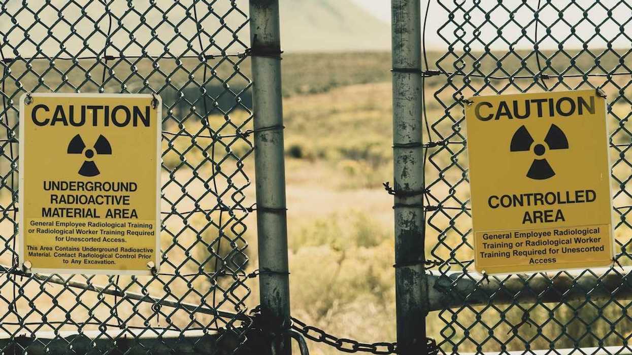 Padlocked gate with signs warning about "Underground Radioactive Material Ahead" against an out of focus background depicting sagebrush and a mountain beyond