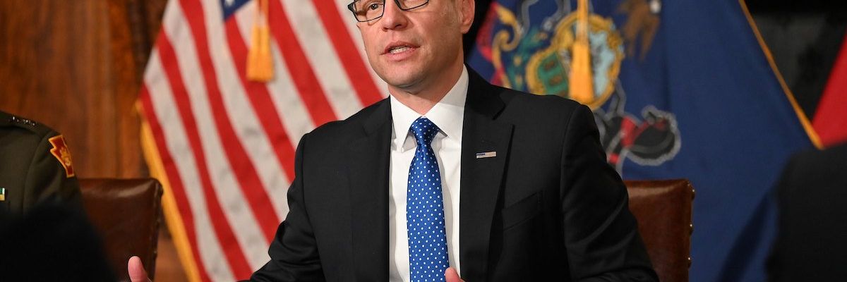 Pennsylvania governor Josh Shapiro speaks with the state flag and American flag behind him.