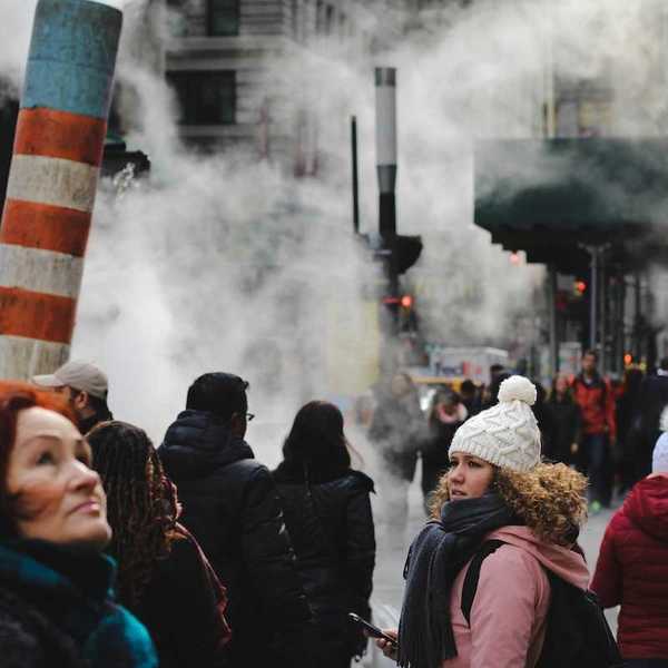People going about their day on a crowded sidewalk in a smoky, smoggy, congested, NYC.