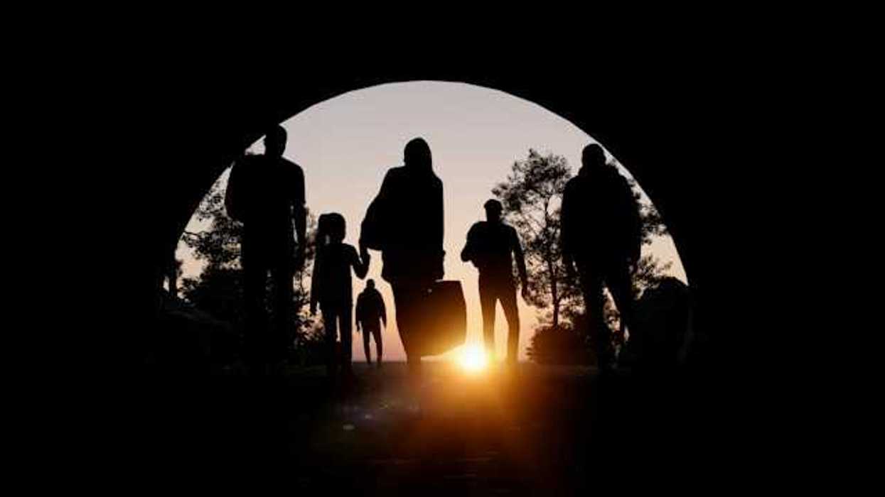 People silhouetted in an arch carrying suitcases and walking toward the setting sun