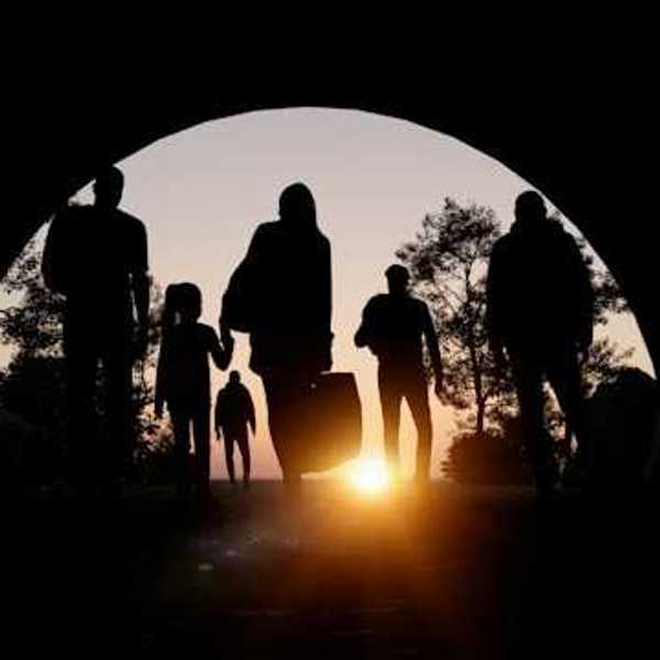 People silhouetted in an arch carrying suitcases and walking toward the setting sun