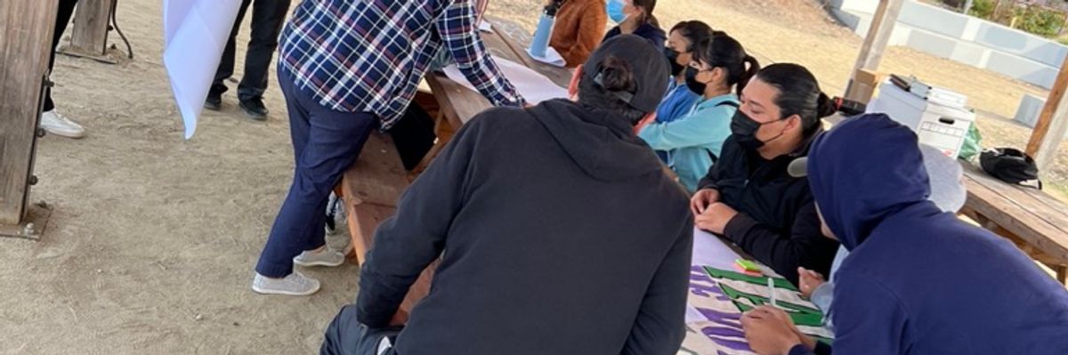 People  sitting in an outdoors table working on a big sign.