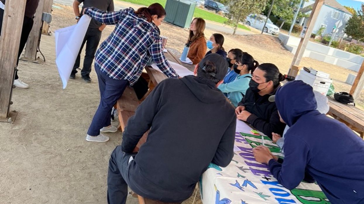 People sitting in an outdoors table working on a big sign.