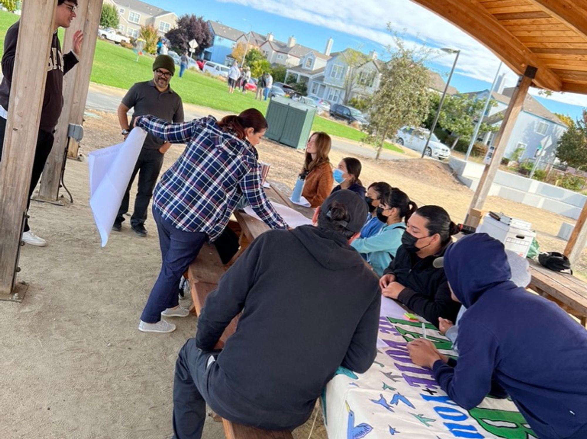 People  sitting in an outdoors table working on a big sign.