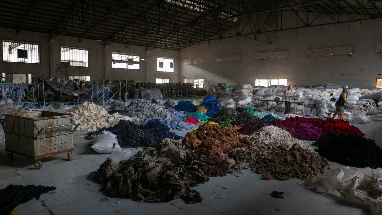 People sorting piles of colorful textile scraps in a large industrial warehouse.