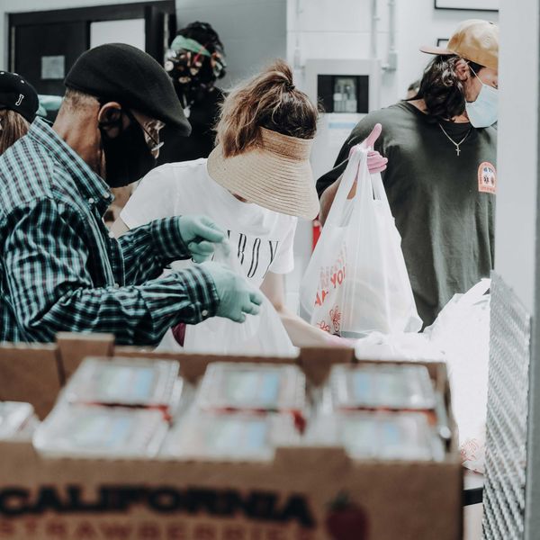 people standing in front of brown cardboard boxes of strawberries.
