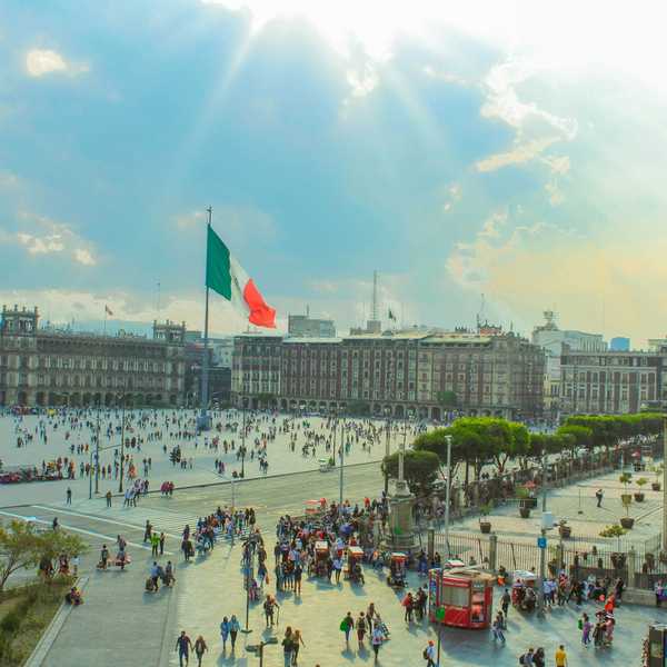 People walking around the Zócalo in Mexico City with large Mexican flag flying.