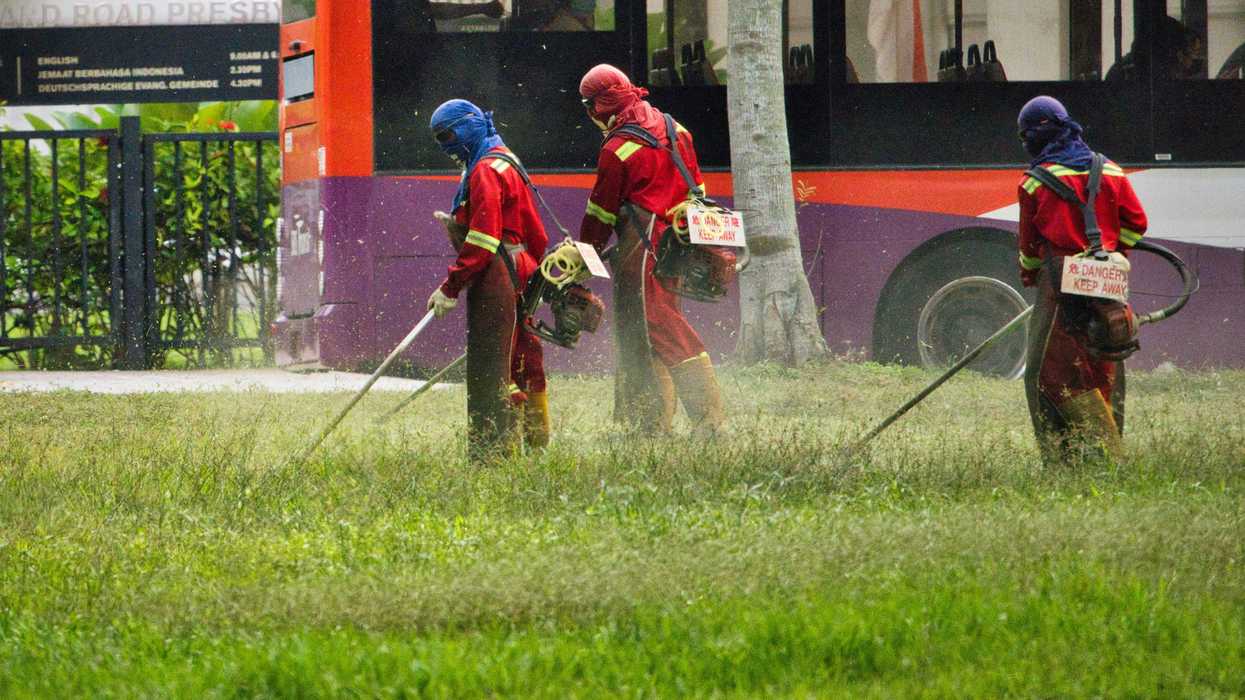 People wearing colorful protective gear and masks spray pesticides in a park.