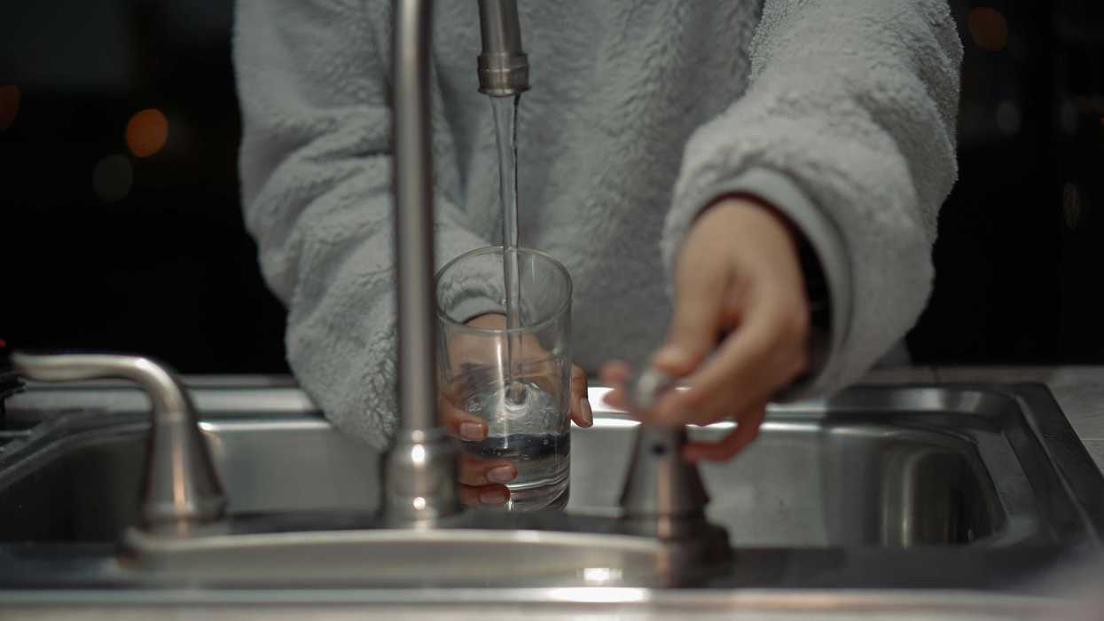 person at sink filling a glass with water.