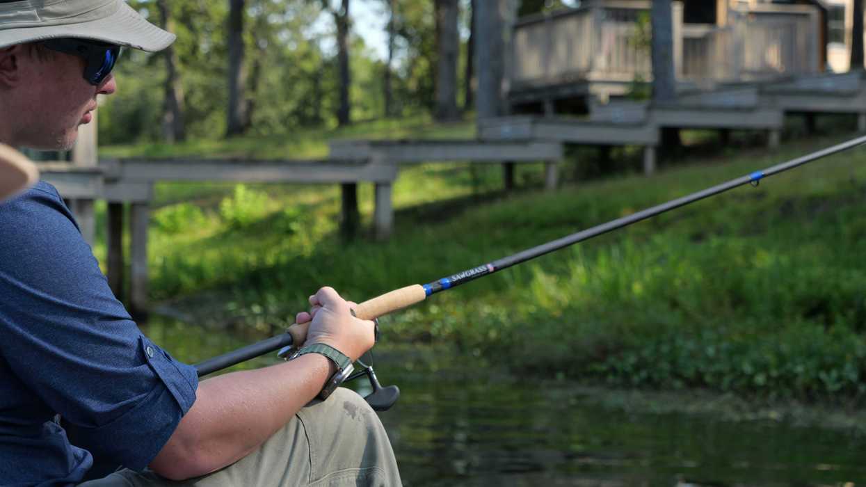 Person fishing from a boat on a lake with a house and dock in background.