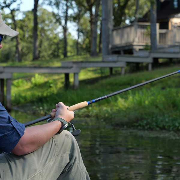 Person fishing from a boat on a lake with a house and dock in background.