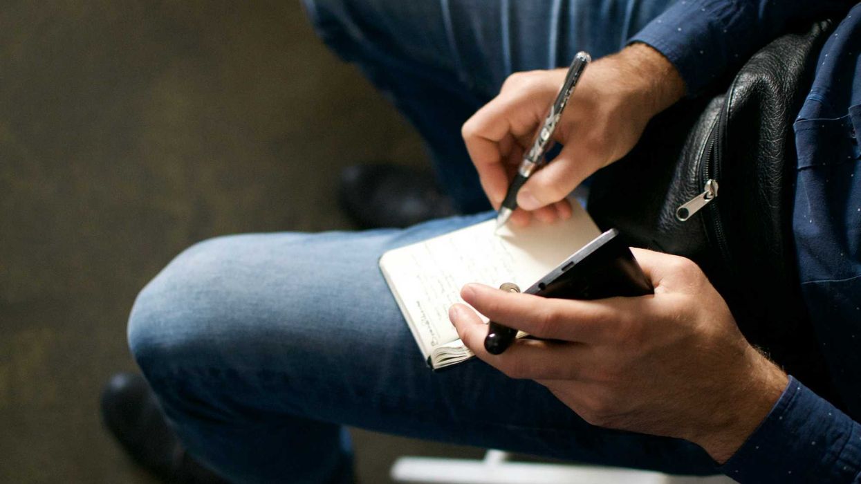 Person holding a cell phone and notepad on their lap while writing.