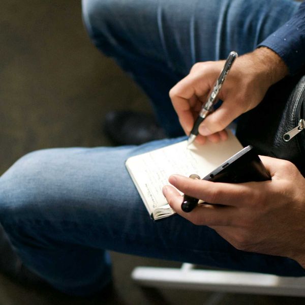 Person holding a cell phone and notepad on their lap while writing.