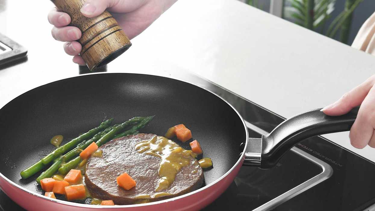 person holding black and red nonstick frying pan cooking meat and veggies.