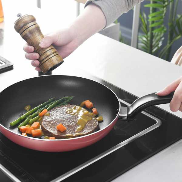 person holding black and red nonstick frying pan cooking meat and veggies.