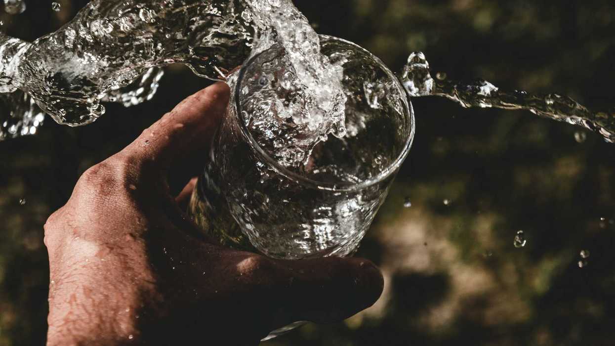 person holding drinking glass with water splashing out.