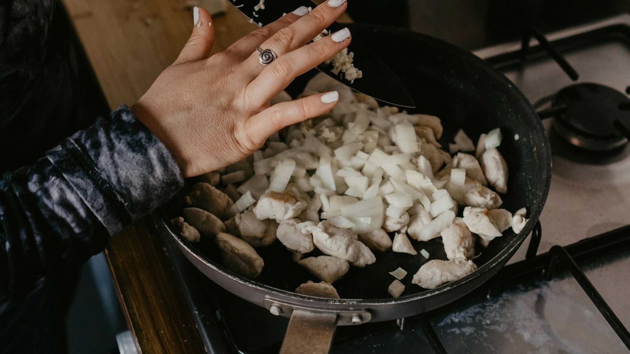 person holding nonstick black frying pan with onions and chicken chunks.