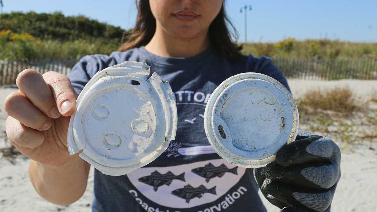 Person holding plastic cup lids on a beach.