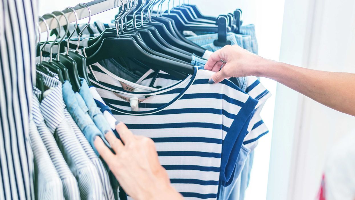 person holding white and black striped shirt on a clothing store rack.