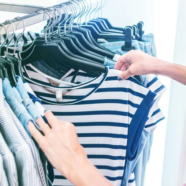 person holding white and black striped shirt on a clothing store rack.