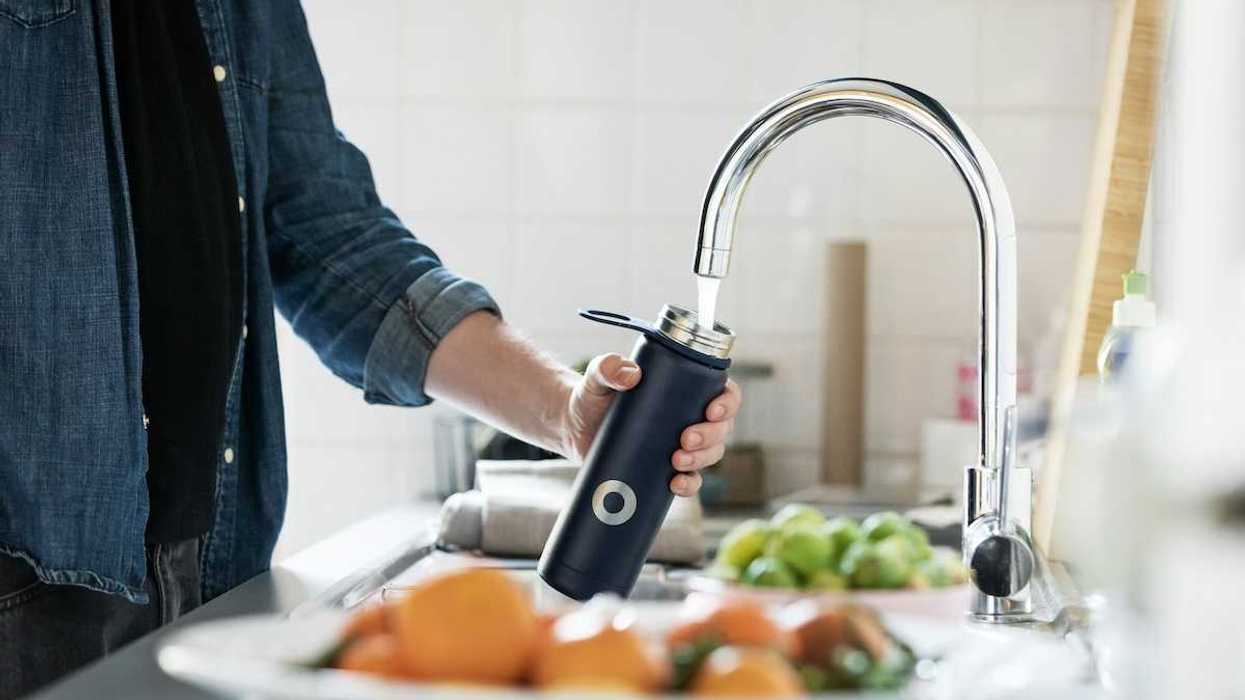 Person in blue denim shirt filling reusable water bottle from tap