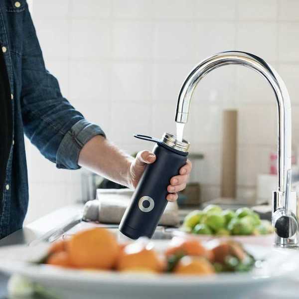 Person in blue denim shirt filling reusable water bottle from tap