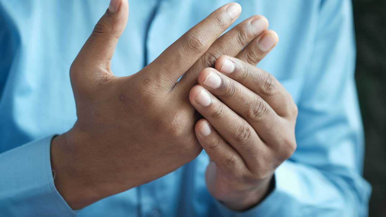 person in blue shirt with one hand holding the knuckles of the other.