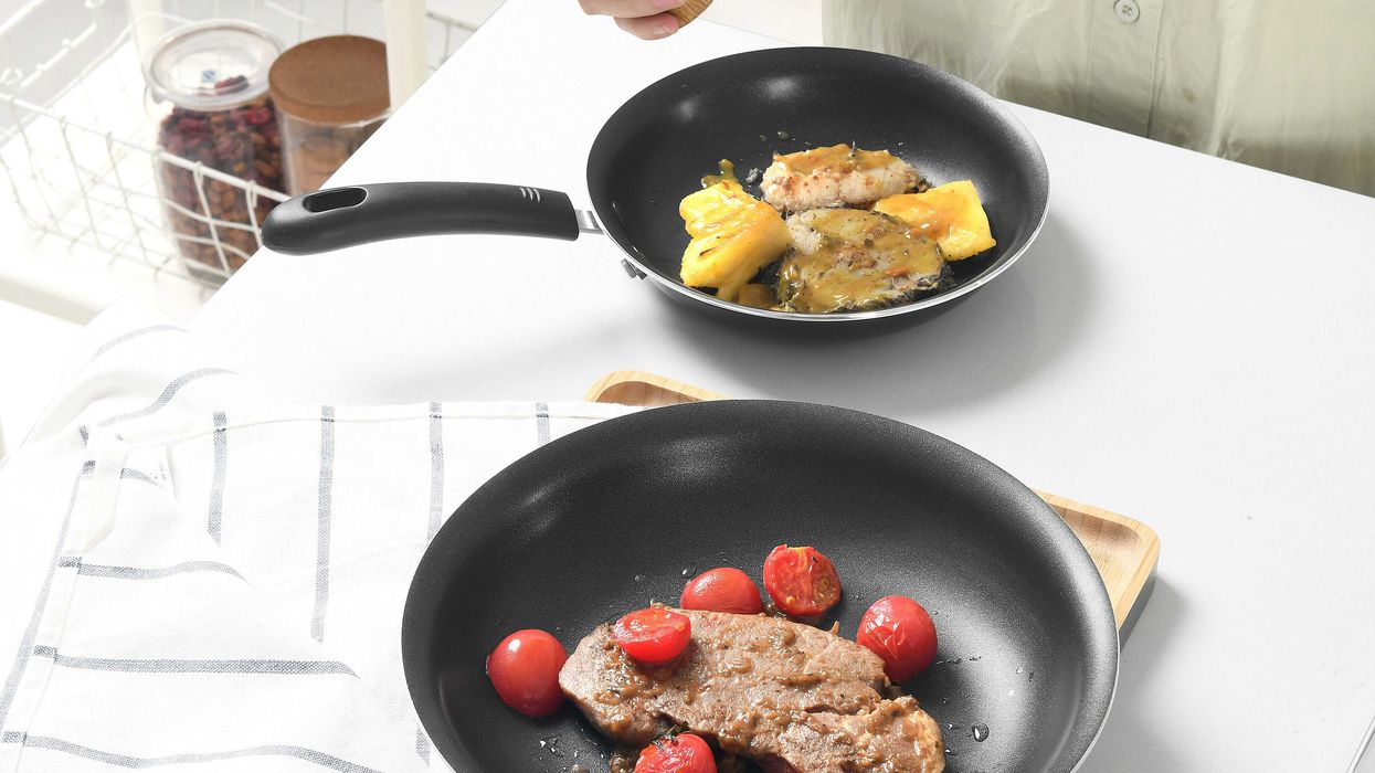 person in front of two black nonstick frying pans with fried foods.