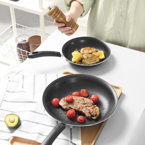 person in front of two black nonstick frying pans with fried foods.