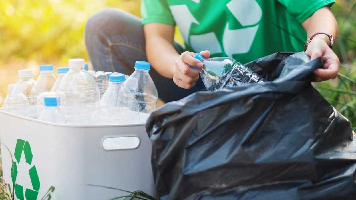 Person in green shirt featuring universal recycling logo sorting plastic boittles from trash bag into recycling container