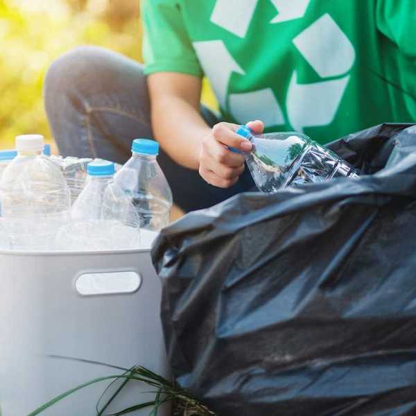 Person in green shirt featuring universal recycling logo sorting plastic boittles from trash bag into recycling container