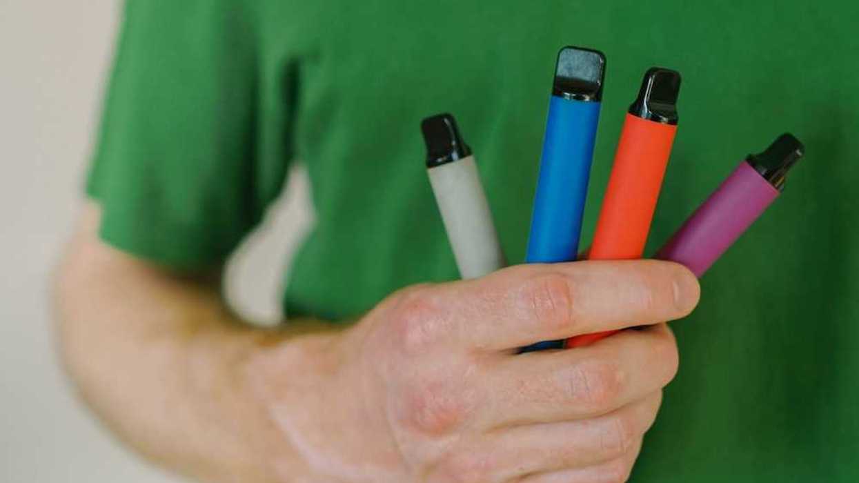 Person in green tee shirt holding four different colored vaping pens