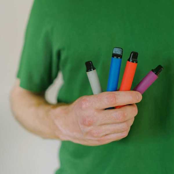 Person in green tee shirt holding four different colored vaping pens