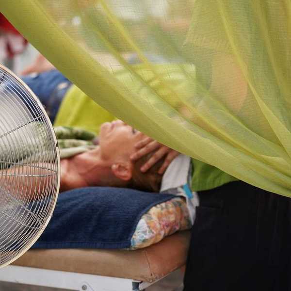 person in supine position receiving massage therapy in front of portable fan