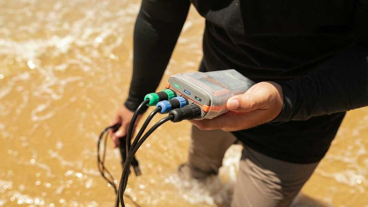 Person, knee-deep in a waterway testing water with an electronic instrument