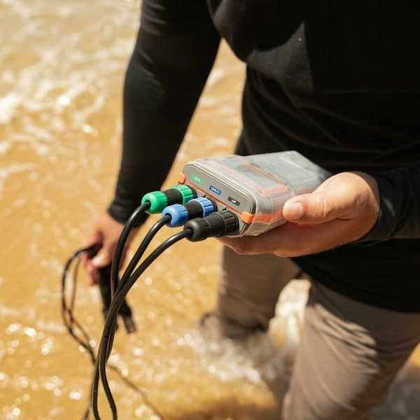 Person, knee-deep in a waterway testing water with an electronic instrument