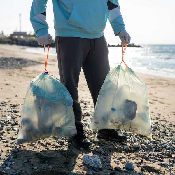 Person on a lakeshore carrying two plastic bags containing collected waste
