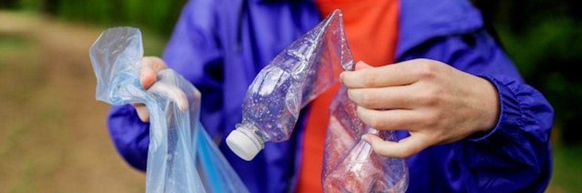 Person placing a plastic bottle into a plastic trash bag.